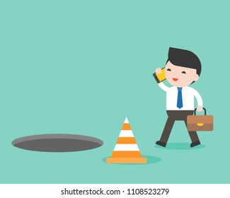 Businessman using cellphone while walking and open manhole on footpath, smartphone addict