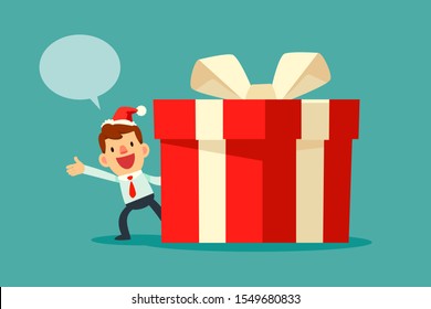 Businessman wearing santa claus hat with dialogue bubble standing beside big red christmas gift box with white ribbon. Christmas celebration. Business announcement concept.