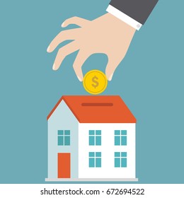 Businessman's hand putting coin inside the house to save money