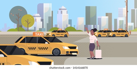 Businesswoman catching taxi on street.  African American business woman with luggage stopping yellow cab. City transportation service concept.  Cityscape background.  Full length,  flat horizontal.