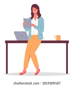 Businesswoman holding digital tablet in hands. Business lady leaning on table with laptop, cup. Confident smiling happy woman brunette wearing pants, blouse, cardigan. Office worker portrait