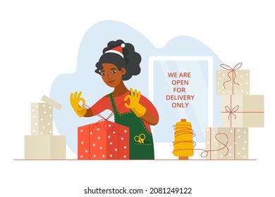 A businesswoman or shop worker wearing a Christmas cap packs orders in wrapping paper as gifts. Small business is open for delivery only. Decorating of New Year presents. 