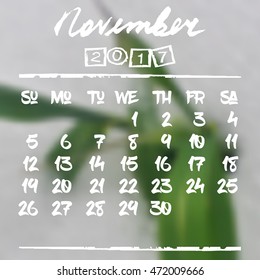 Calendar design grid in hand written style with white lettering and dates of autumn month November 2017 on natural blurred background. Blurry green leaf in snow. Vector illustration