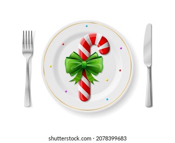 Candy cane is on white plate with fork and knife, top view. Dinner plate with candy stick inside and cutlery set on sides