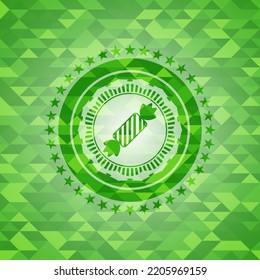 candy icon inside green emblem with triangle mosaic background. 