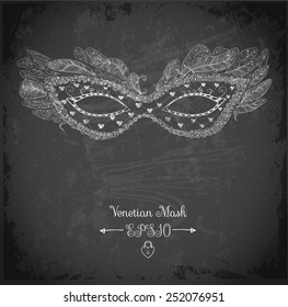 Card with festive venetian mask decorated with feathers on black chalkboard