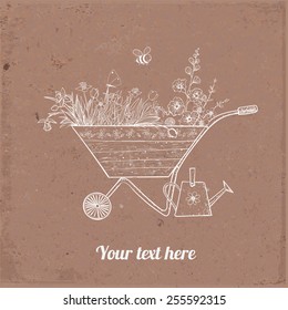 Card with old wooden garden cart full of spring flowers and little watering can under it on brown parcel paper