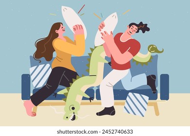 Carefree couple fights with pillows, sitting on sofa, enjoying pleasure of relaxing together in cozy home atmosphere. Cheerful brother and sister fight with pillows enjoying having free time