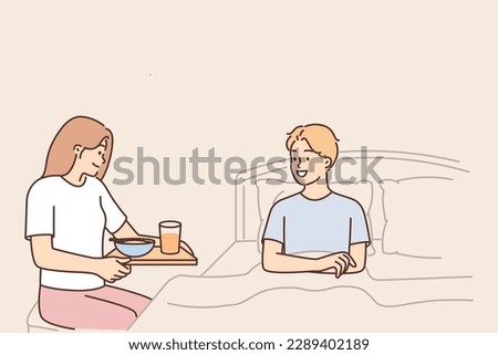 Caring wife brings breakfast to bed to beloved husband, wanting to bring joy or caring during illness. Young cheerful family couple spend time together on weekend and have breakfast in bedroom