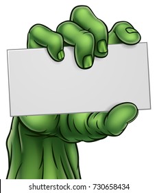 A cartoon green zombie Halloween monster claw hand holding blank paper sign or card