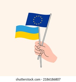 Cartoon Hand Holding European Union And Ukrainian Flags. EU Ukraine Relationships. Concept of Diplomacy, Politics And Democratic Negotiations. Ukraine as Independent Nation and EU Member Candidate. 