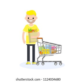Cartoon illustration - a young guy with a beard in a yellow shirt stands next to a grocery cart with products-cheese, sausage, boxes. man holding a paper bag with vegetables and bread. shopping mall