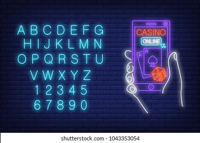 Casino online neon sign. English alphabet and numbers. Hand holding smartphone with dice and playing cards. Night bright advertisement. Vector illustration in neon style for internet gambling and luck