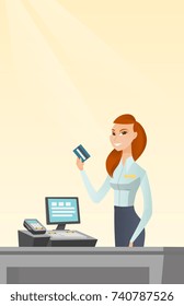 Caucasian smiling cashier standing at the checkout and holding a credit card. Young cheerful cashier making payment by credit card. Vector flat design illustration. Vertical layout.