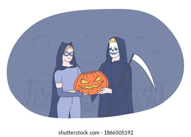 Celebrating Halloween holiday in spooky costumes concept. Young people cartoon characters in witch and death costume holding pumpkin in hands over cemetery at darl background 