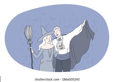 Celebrating Halloween holiday in spooky costumes concept. Young positive couple in festive costumes of witch and dracula standing holding skull in hands over flying bats at dark background 