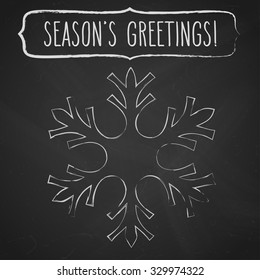 Chalk snowflake and a frame with hand written season's greetings over black chalkboard.