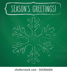 Chalk snowflake and a frame with hand written season's greetings over green chalkboard.