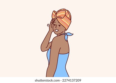 Charming African American woman with traditional turban on head is dressed in blue dress for going to ethnic party. African girl smiling and looking at screen demonstrating fashion national minorities