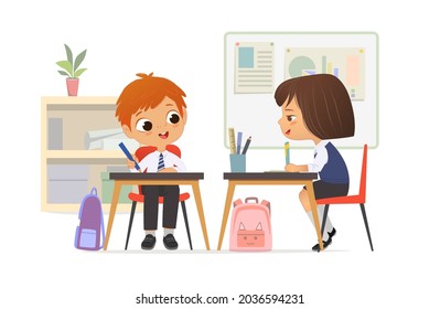 Cheerful elementary classmates wearing school uniform talking at lesson sitting at table with stationery vector flat illustration. Cute schoolboy and schoolgirl studying at primary classroom together