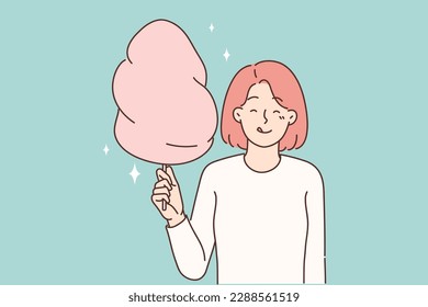 Cheerful girl with cotton candy in hands licks lips in anticipation taste of street dessert bought during walk in park. Positive woman holding appetizing sweet cotton candy for happy childhood concept