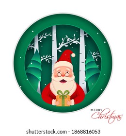 Cheerful Santa Claus Character Holding a Gift Box on Green and White Paper Cut Nature Background for Merry Christmas Celebration.
