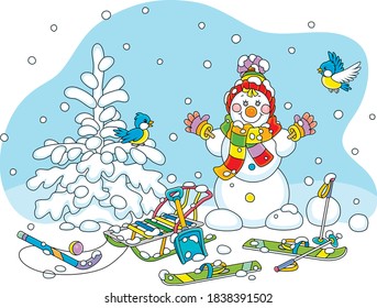 Cheerful small birds flying around a smiling cute toy snowman with a warm colorful scarf and a hat, skis and a sledge on a snowy playground in a white winter park, vector cartoon illustration