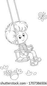 Cheerful small boy swinging on a summer playground in a park, black and white outlined vector cartoon illustration for a coloring book page