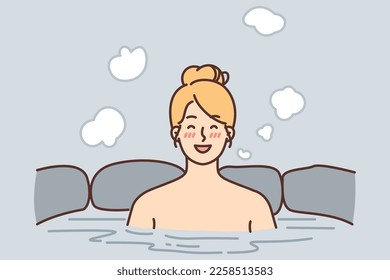 Cheerful woman relish spa treatments and hot beauty bath surrounded by natural stone. Girl visitor of spa center bathes sitting in healing water and smiles enjoying long-awaited vacation