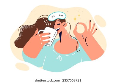 Cheerful woman in sleep mask drinks coffee and shows OK gesture, rejoicing at start of new working day. Cheerful and energetic girl waking up early in morning is ready to perform professional tasks