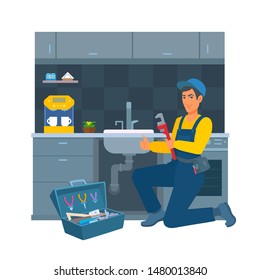 A cheerful worker in a blue uniform and cap with a pipe wrench in their hand. Kitchen on the background. A happy male professional plumber kneels near a sink, showing gesture thumb up, smiling.