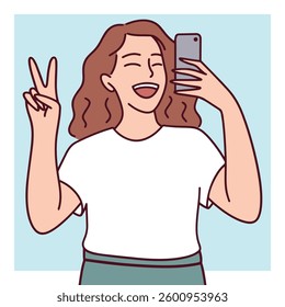 A cheerful young woman holding a smartphone and taking a selfie while making a peace sign. A concept of social media, happiness, and self-expression.