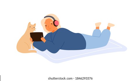 Niño con auriculares tirado en el suelo con un gato lindo y viendo una película en una tableta juntos. Acogedora escena casera con una chica que se relaja con un bonito gatito. Caricatura vectorial plana ilustra aisladamente el blanco.