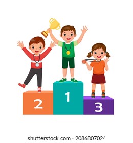 Children with medals holding gold cup trophy standing on winners podium or pedestal  with first, second and third place prize celebrating winning competition