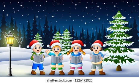 Children singing christmas carols in winter chlotes and santa hat with snowy pine background