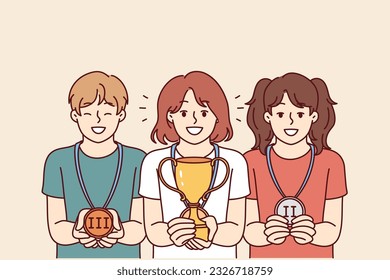 Children with trophies for winning school olympiads or competitions rejoice in awards for leadership positions. Girl with winner cup stands near classmates with medals out for winning competition