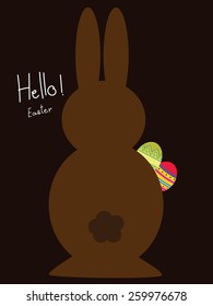 Chocolate bunny holding Easter eggs on dark background.