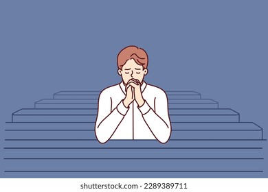 Christian man sits and prays in catholic church, turning to god to confess or ask for help. Believing guy in church and prays to feel psychological relief or observe religious ritual 