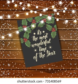 Christmas background with greeting card and garlands on wooden board. Hand made quote "It's the most wonderful time of the year". Festive background. Lettering, sketch. Banner, poster, brochure.