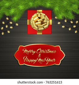 Christmas card with Cristmas fir tree branches, red square gift box with gold ribbon bow, garland on black wooden board. Greeting text Merry Chrismas and Happy New Year on red label with gold frame