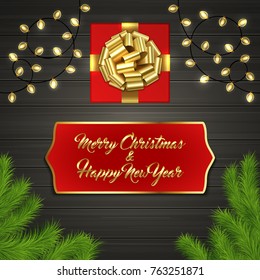 Christmas card with Cristmas fir tree branches, red square gift box with gold ribbon bow, garland on black wooden board. Greeting text Merry Chrismas and Happy New Year on red label with gold frame