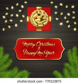 Christmas card with Cristmas fir tree branches, red square gift box with gold ribbon bow, garland on black wooden board. Greeting text Merry Chrismas and Happy New Year on red label with gold frame