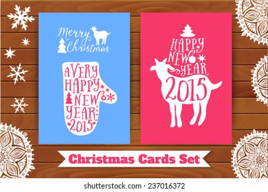 Christmas card set. Goat and mitten with lettering elements, on table top. Decorated with paper snowflakes