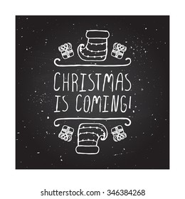 Christmas is coming  - christmas typographic element. Hand sketched graphic vector element with text, gifts and sock on chalkboard background.