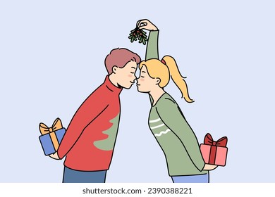 Christmas couple with gift boxes kisses and holds fir cones in hands, preparing to exchange new year presents. Husband and wife in christmas sweaters celebrate winter holidays together