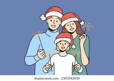 Christmas family of dad with mom and smiling child use sparklers celebrating new year holidays. Young parents and daughter in christmas santa hat wishing happy yuletide and xmas holiday