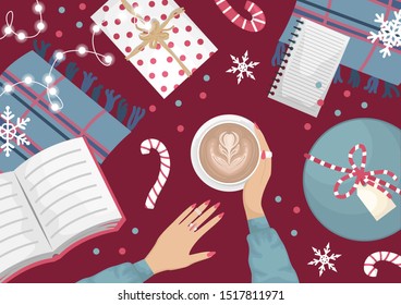 Christmas flat lay with a wool wardrobe, a book, a garland and Christmas gifts. Girls hands with a cup of cappuccino