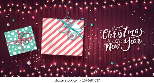 Christmas garlands of lights, two gift boxes, baubles and confetti. Holiday background with presents, glowing LED light bulbs on purple knitted texture. Xmas decorations for new year card, poster