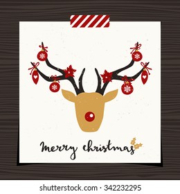 Christmas greeting card template design on wood background. A deer head decorated with red Christmas baubles on snowflake pattern background. Hand lettered text "Merry Christmas".