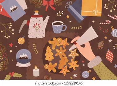 Christmas greeting card template with hand holding pastry bag and decorating cookies, cup of tea, teapot and festive seasonal decorations lying on table. Colorful vector illustration in flat style.